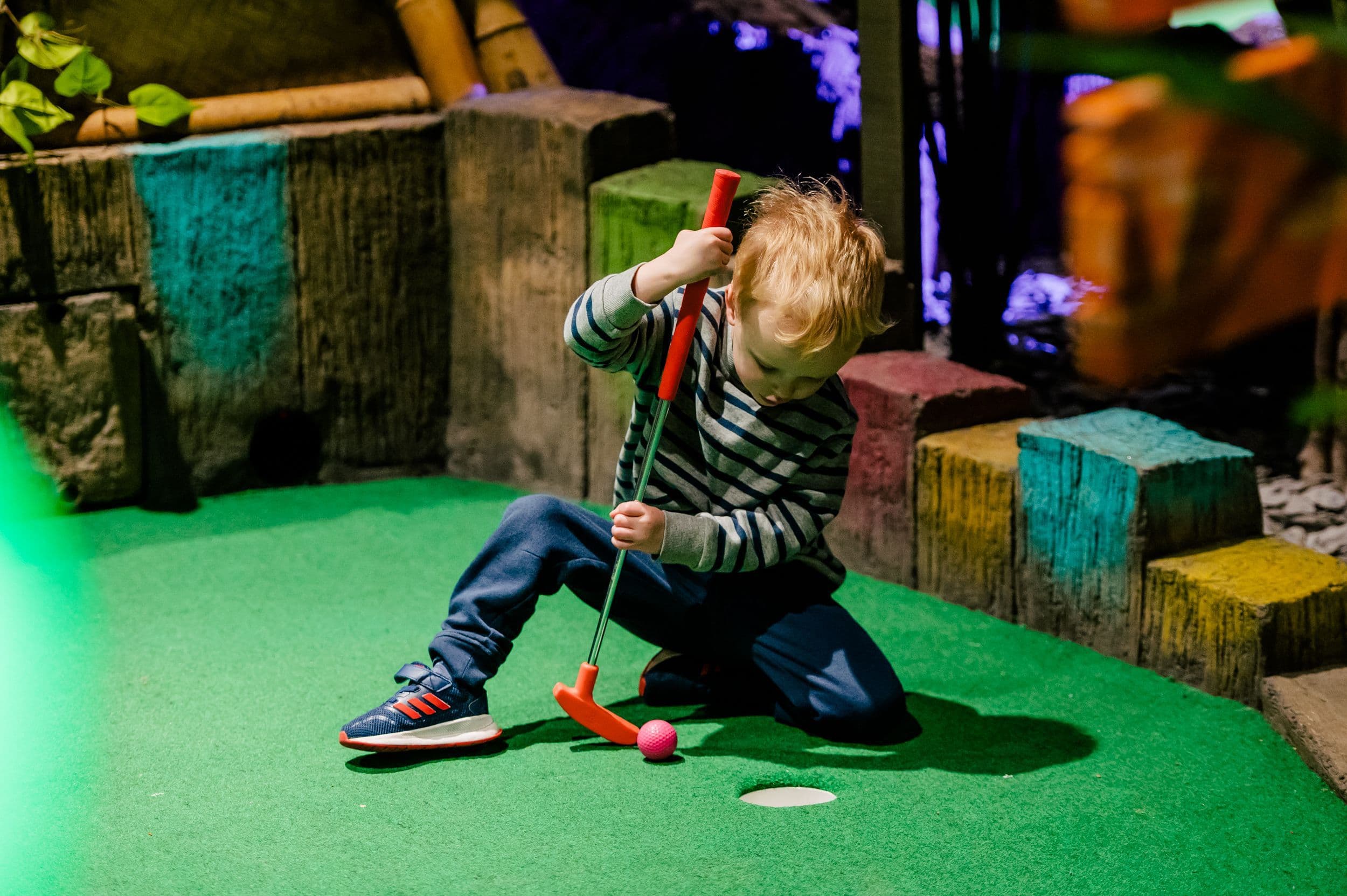A small toddler kneeling down to hit the mini golf ball.